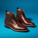 A pair of brown leather lace-up ankle boots with dark gray elastic side panels, displayed on a vibrant blue studio background.