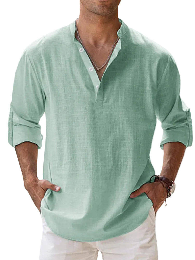 Man wearing a light green shirt with rolled-up sleeves against a blurred background