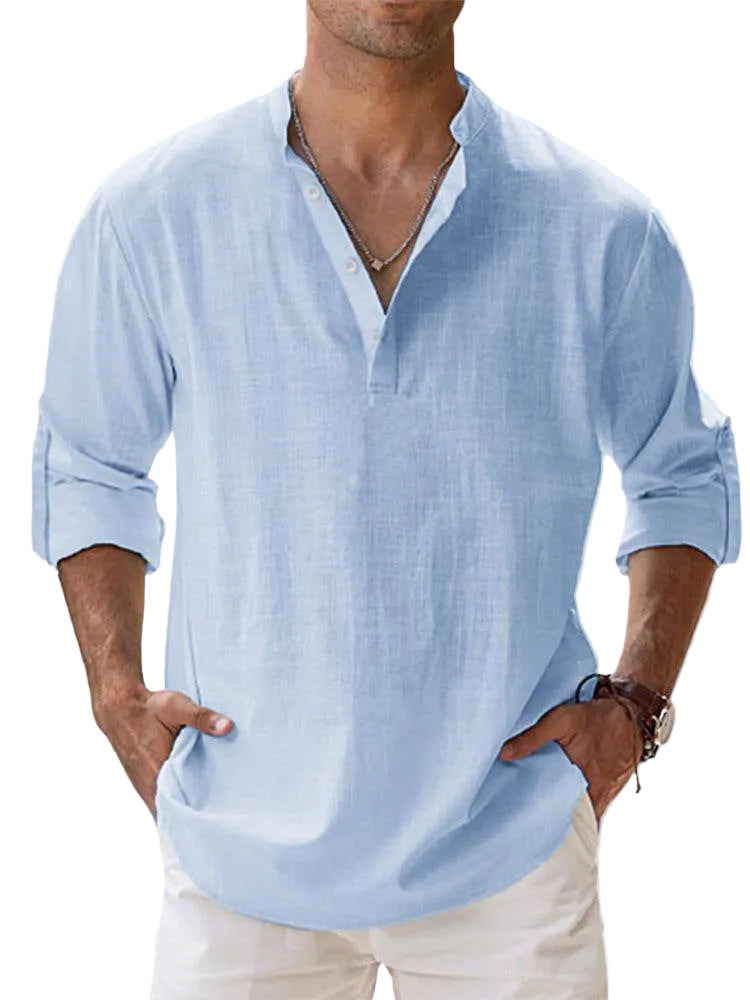 Man wearing a light blue shirt with rolled-up sleeves against a blurred outdoor background