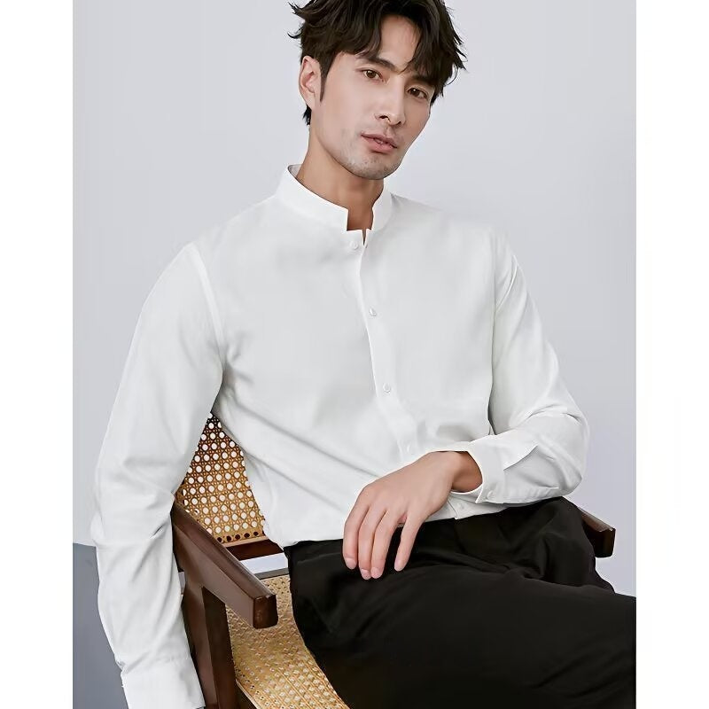 Man wearing a white shirt and black pants sitting on a wooden chair against a plain background