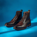 A pair of dark brown leather lace-up ankle boots with cap toes, displayed on a vibrant blue studio background.