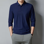 Person wearing a navy long-sleeve polo shirt and gray pants against a gray background